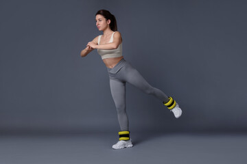 Wall Mural - Woman in sportswear exercising with ankle weights on grey background