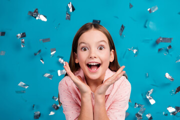 Wall Mural - Excited young girl celebrating with a joyful face and confetti flying on a vibrant blue background