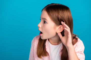 Wall Mural - Young girl with curious expression listening attentively against blue background in a pink polka-dot shirt