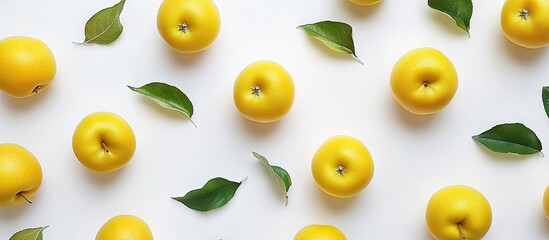 Wall Mural - Vibrant yellow apples scattered on a clean white background with green leaves accentuating their freshness and enticing appetizing appearance.