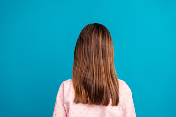 Wall Mural - Stylish young girl with long brown hair in casual pink shirt against bright blue background, back view