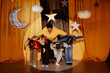 © Seventyfour - Group of children, led by their teacher, bowing to audience on stage decorated with stars and moon cutouts. Performance expressions showing pride and joy