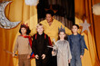 © Seventyfour - Group of children wearing costumes and standing on stage with stars hanging, assisted by an adult smiling behind them. Background features moon and stars made from paper