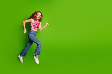 Wall Mural - Cheerful young lady with curly red hair posing energetically against a solid green background