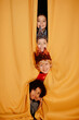 © Seventyfour - Group of children peeking from yellow curtain during holiday performance, smiling and showing enthusiasm for the event. Four kids in costume portraying excitement and joy