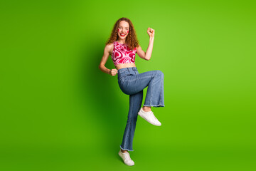 Wall Mural - Excited young woman with curly red hair dancing cheerfully on a bright green background