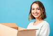 © Leonardo - Mujer joven sonriente sosteniendo una caja de cartón abierta aislada sobre fondo azul