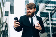 © BullRun - Confident businessman using smartphone on city street