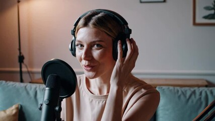 Poster - Woman content creator wearing headphones recording podcast, adjusting microphone and smiling while sitting comfortably in home studio during digital media production