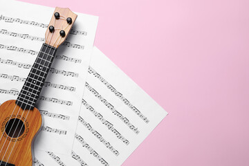 Wall Mural - Ukulele and music sheets on pink background, top view. Space for text