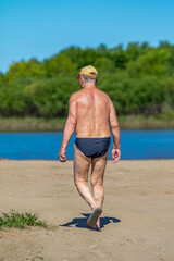 Wall Mural - A man walks on a beach wearing a yellow hat and a black swimsuit