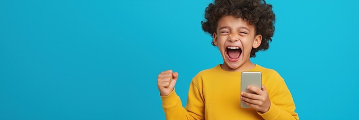 Wall Mural - A young boy is holding a cell phone and smiling. Concept of happiness and excitement, as the boy appears to be celebrating or sharing a joyful moment with the phone