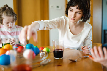 Wall Mural - Pretty teenage girl dyeing Easter eggs at home. Child painting colorful eggs for Easter hunt. Kid getting ready for Easter celebration.