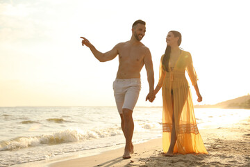 Wall Mural - Happy young couple walking together on beach at sunset