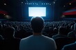© Andrii Zastrozhnov - A man is sitting in a movie theater with a large crowd of people. The theater is dark and the man is looking at the screen