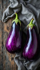 Two vibrant heirloom eggplants resting on rustic wood and linen fabric