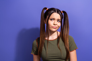 Wall Mural - Young woman with ponytails expressing a thoughtful look in front of a purple background