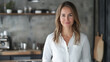 © GrayFrog - Confident woman in a white shirt stands in a modern industrial style kitchen and smiling warmly at the camera.
