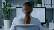 © Jaroon - Focused on the Task: A woman sits at her desk, immersed in work, her back to the camera, her focused gaze on a computer monitor. The office space exudes an air of quiet determination.