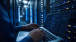© mahamad - A computer engineer working on a laptop in a server room, representing a data center focused on big data storage�ideal for IT support and telecommunication concepts.