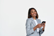 © insta_photos - Smiling happy African American young adult business woman entrepreneur wearing suit holding smartphone in hands using mobile apps on cellphone standing isolated on white background looking at camera.