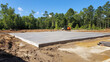 © Kosin - cement slab being poured for new foundation in construction site surrounded by trees and clear blue skies. scene conveys sense of progress and development
