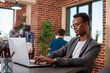 © DC Studio - Male entrepreneur works diligently on financial research using his laptop in startup office. Black businessman at desk with his personal computer is focused on improving company status growth.