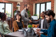 © DC Studio - Caucasian man greets african american manager during meeting in brick wall workspace. Businessmen shaking each others hands at table as their coworkers prepare for group discussion in startup office.