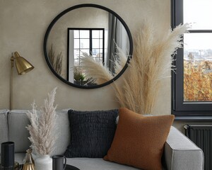 Wall Mural - Modern living room interior featuring a round mirror with a black frame, dried pampas grass, and textured throw pillows on a couch. View of a window