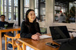 © Wasana - A woman is sitting at a table with a laptop and a notebook