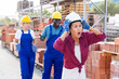 © JackF - Three builders standing in outdoor construction material storage. Taskmaster in white hardhat amazed by something she just saw.