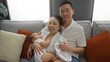 © Krakenimages.com - Family portrait showing an asian couple with baby in cozy living room, highlighting mother, father, and toddler with warmth, happiness, and love indoors.