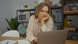 © Krakenimages.com - Woman working on laptop in modern office setting with blonde hair, focused expression, surrounded by office supplies, indoor plants, and kitchen items in the background.