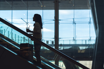 Wall Mural - Silhouette standing woman to transit with travel luggage on escalator at international airport terminal