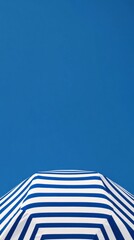 Poster - Beneath the expansive blue sky, a vibrant striped beach umbrella offers shade, inviting relaxation and blissful moments at the coast. Perfect for enjoyment and leisure