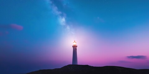 A lighthouse is lit up in the night sky. The sky is a deep blue with a few clouds