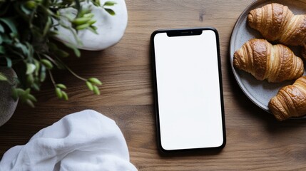 Poster - modern smartphone with a white screen mockup on a wooden countertop, next to a plate of croissants.