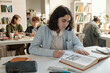 © Mediaphotos - Portrait of young man with long curly hair as student sitting at desk in college library and writing in notebook preparing for exams copy space