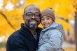 © Thali - A photo of an African American father hugging his son, both smiling with joy and happiness in the park on autumn day
