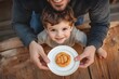 © Thali - A happy little boy with his father. The child holds out to him an apple honey cookie on a white plate and smiles at the camera