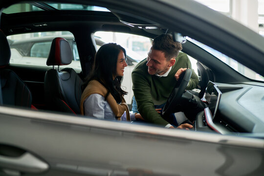 Young couple examines the interior features of a car at a dealership. They are smiling and discussing the vehicle's details, showcasing interest in purchasing a new automobile