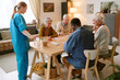 © AnnaStills - Wide shot of nurse pouring water while group of biracial senior people playing bingo at table
