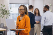 © anatoliycherkas - African american businesswoman holding a laptop, diverse business professionals collaborating, using digital devices and sharing ideas during team meeting in modern, bright workplace