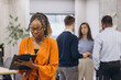 © anatoliycherkas - African american businesswoman holding a folder, professional team collaborating, working together in sleek open plan workspace, representing multicultural corporate synergy