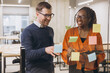 © anatoliycherkas - Professional colleagues collaborating, writing ideas on glass wall with sticky notes, demonstrating creative teamwork in modern office environment