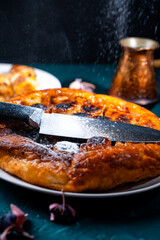 Wall Mural - Put a knife on the pie and sprinkle powdered sugar on top to get the contour of the knife on the pie. On a dark background, powdered sugar falls on a banana tart