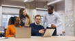 © anatoliycherkas - Group of professionals engaging in a collaborative discussion around laptops in a contemporary office space, highlighting teamwork and diversity