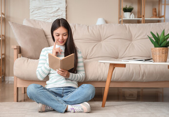 Wall Mural - Beautiful young woman reading book and sitting on floor at home