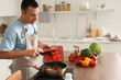 © Pixel-Shot - Young man putting cut bell pepper into frying pan in kitchen