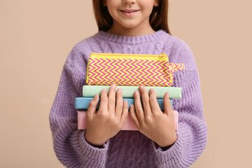 Wall Mural - Cute little happy girl with pencil case and books on beige background, closeup